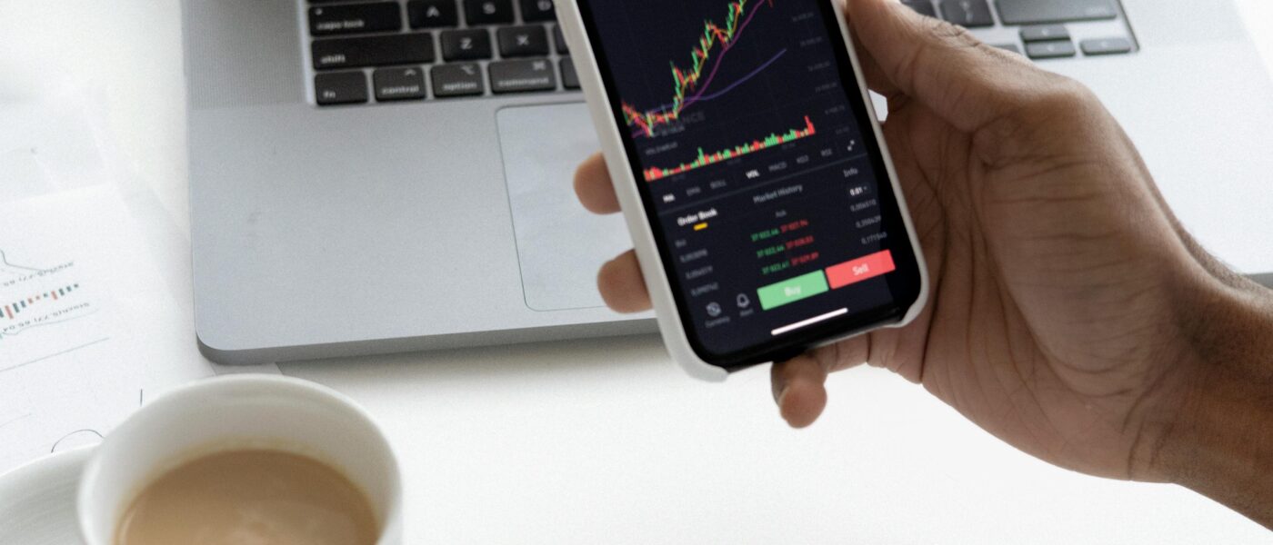 Person analyzing stock market trends on smartphone with laptop background