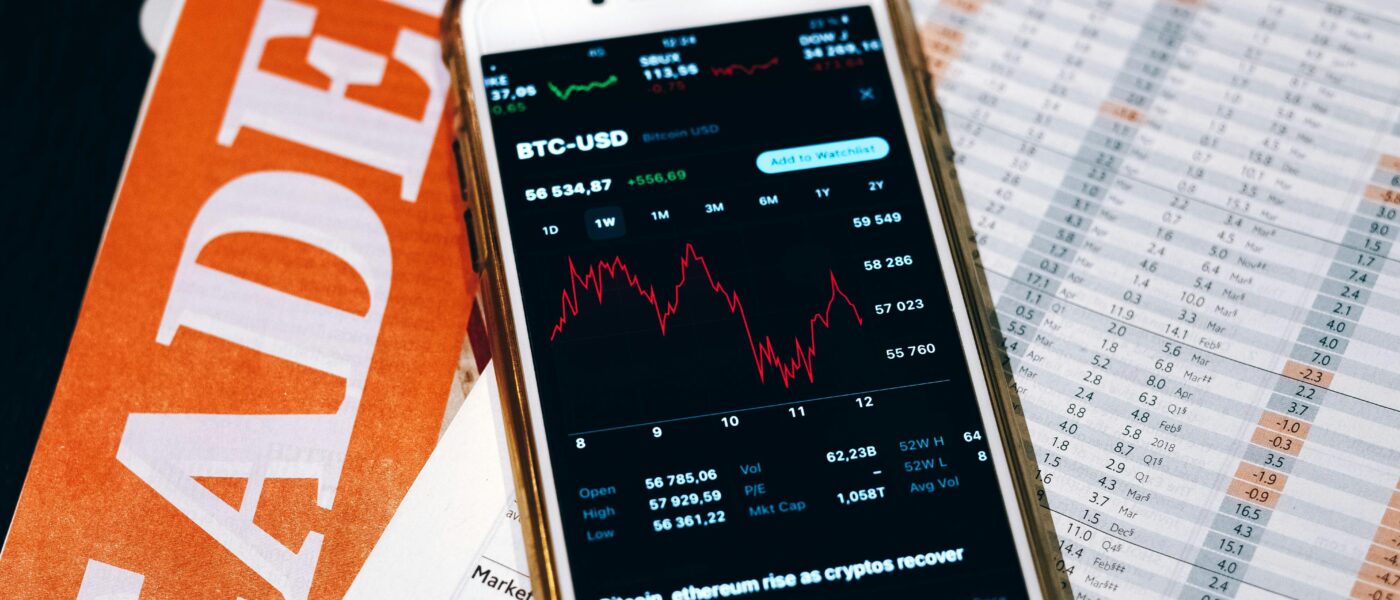 Smartphone displaying BTC chart on financial papers and laptop.