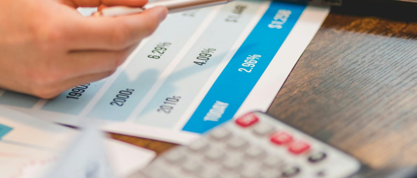 Close-up of a hand using a ballpen and calculator to analyze interest rates on a chart.