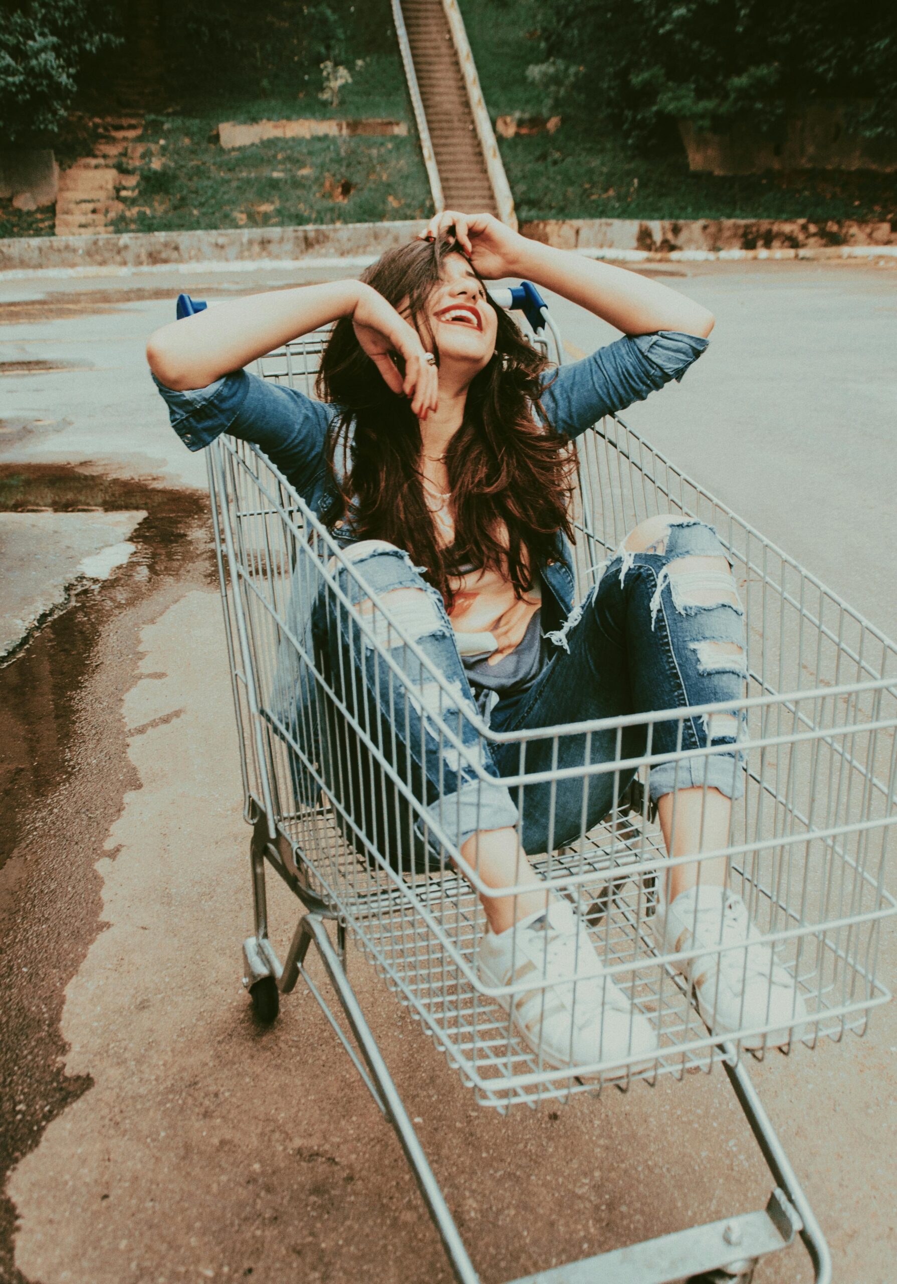 Carefree young woman having fun sitting in a shopping cart outdoors, exuding joy and laughter.