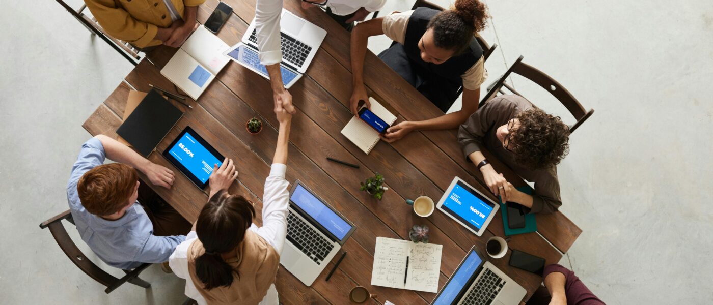 Top view of a diverse team collaborating in an office setting with laptops and tablets, promoting cooperation.