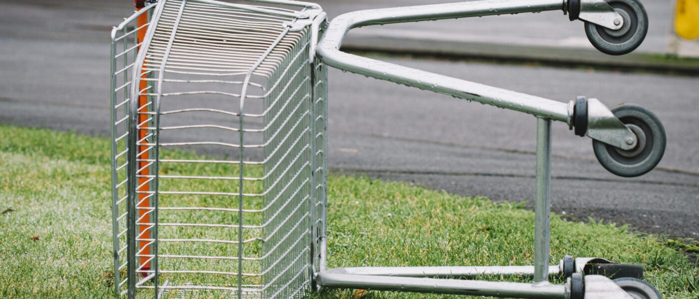 An empty shopping cart lies abandoned on a patch of grass by the roadside.