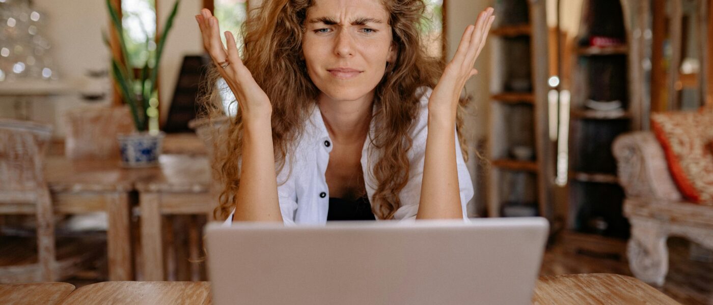 A woman frustrated with her laptop while working remotely indoors, expressing stress.