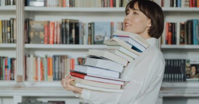 A woman joyfully holds a pile of books in a library, embodying the love of reading and learning.