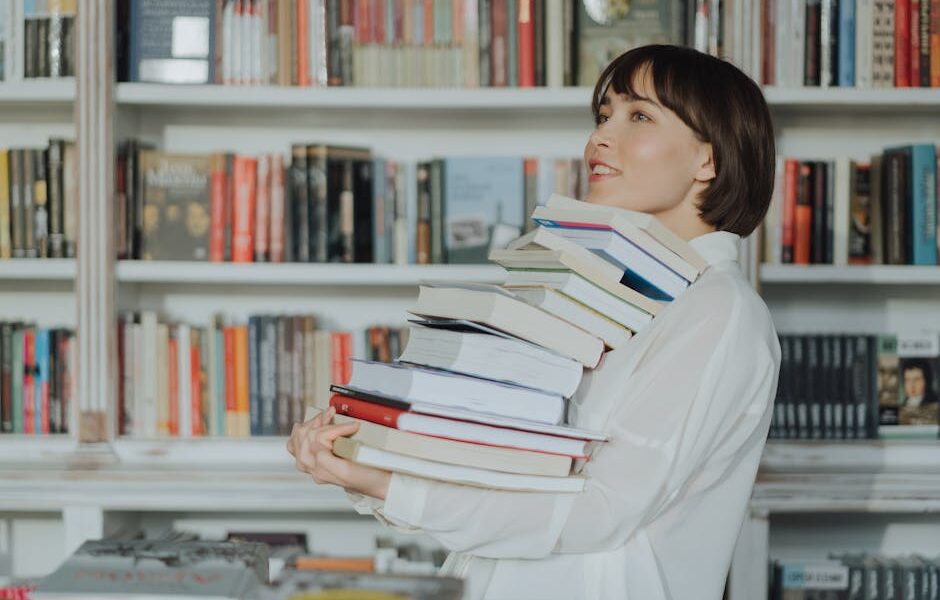 A woman joyfully holds a pile of books in a library, embodying the love of reading and learning.