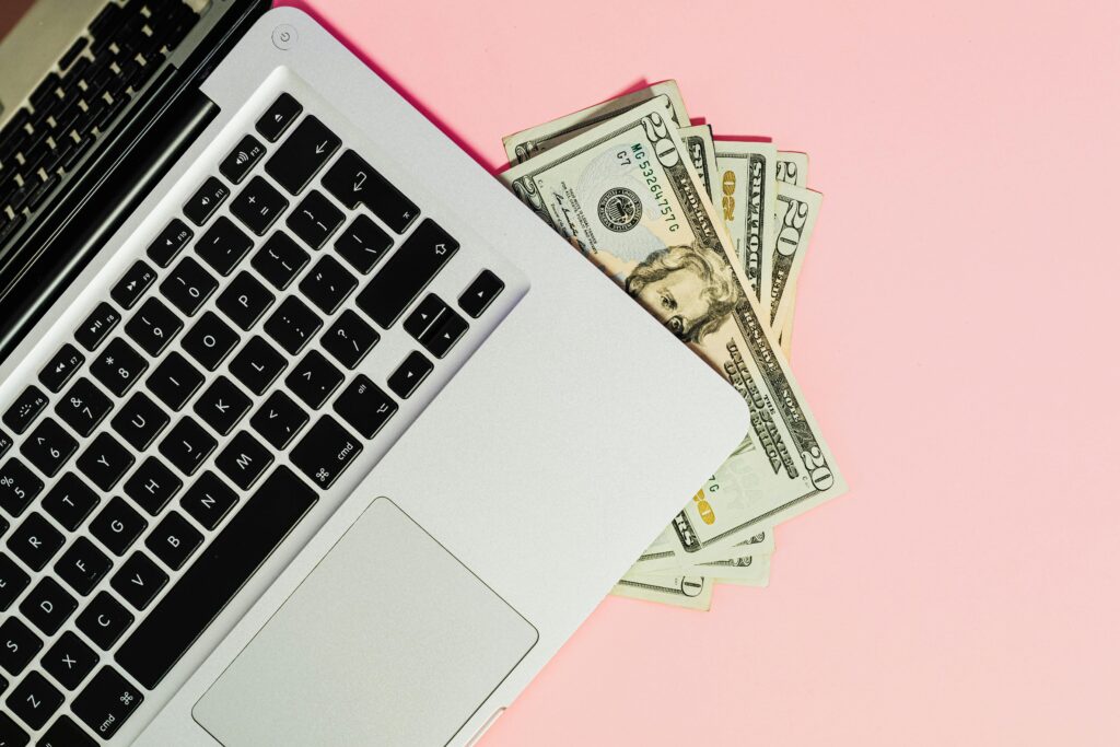 A laptop keyboard with dollar bills on a pink surface, symbolizing online business.