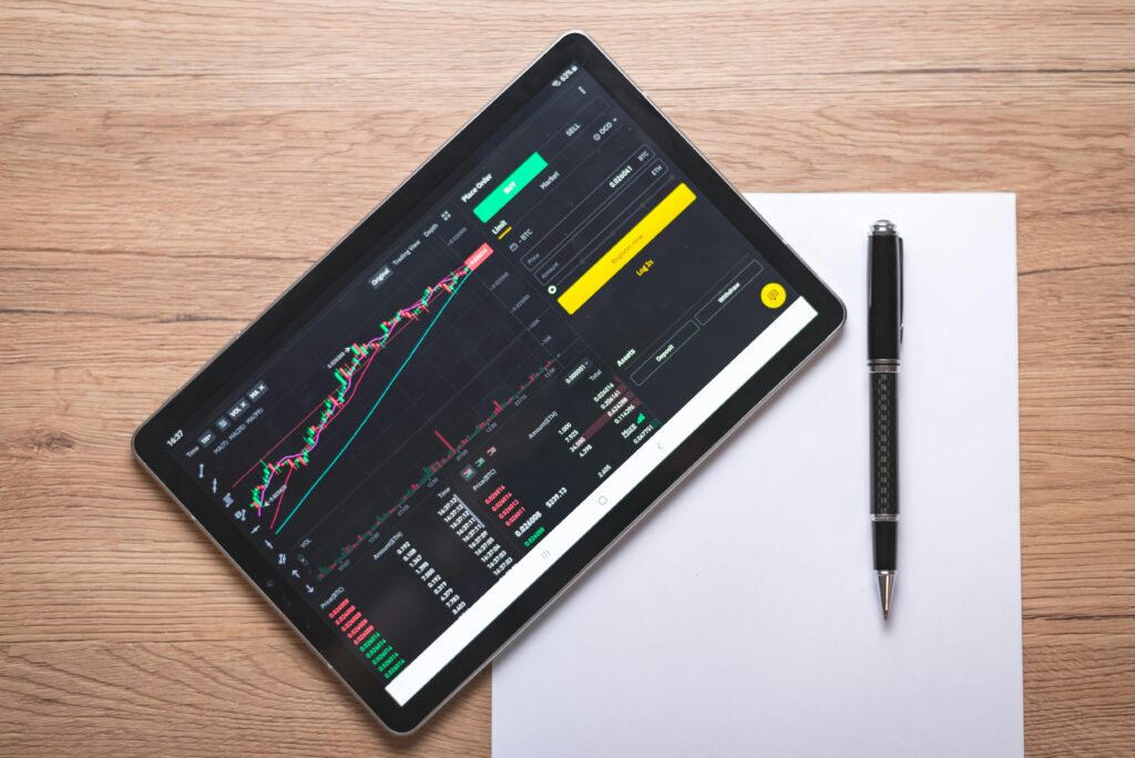 Overhead view of a digital tablet displaying stock market graphs and data on a wooden desk.