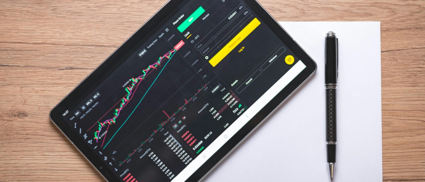 Overhead view of a digital tablet displaying stock market graphs and data on a wooden desk.