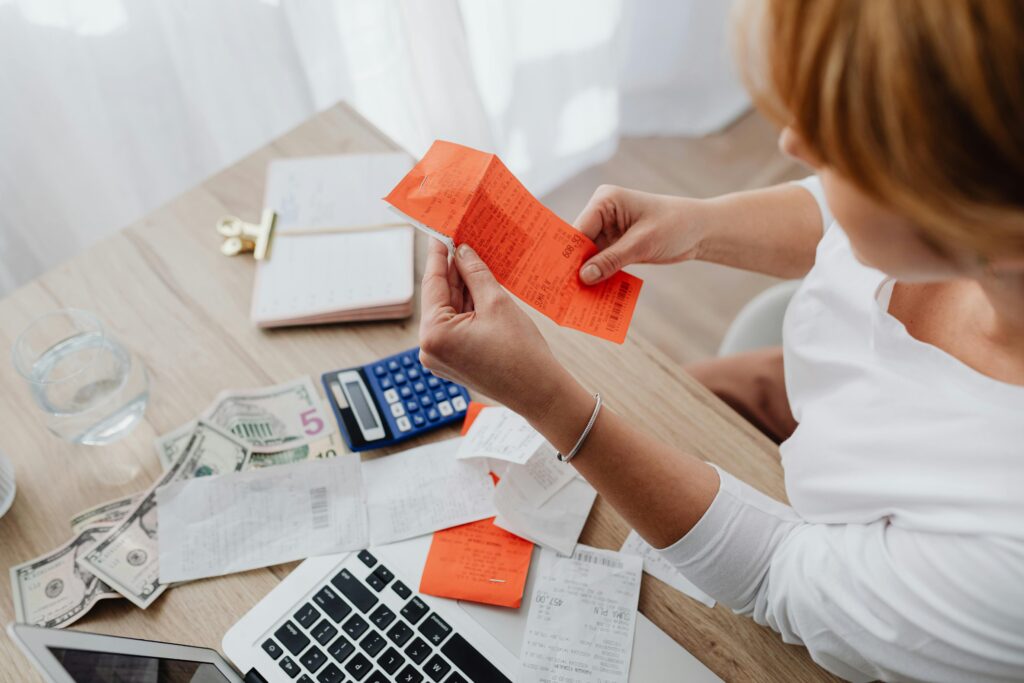 Woman using calculator and receipts at home office desk for finance management.