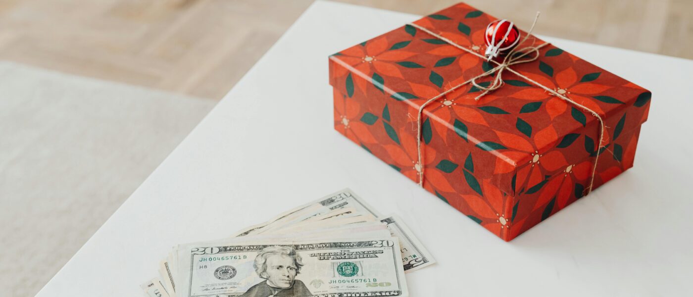 A holiday-themed gift box with US dollar bills on a white table indoors.