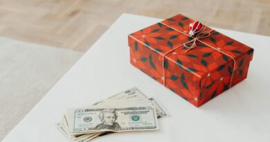 A holiday-themed gift box with US dollar bills on a white table indoors.