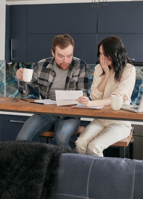 A worried couple reviewing financial documents at their kitchen table.