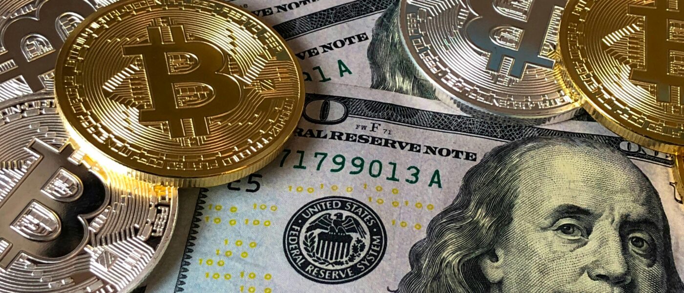 A close-up photo depicting Bitcoin coins on top of US dollar bills, symbolizing finance and cryptocurrency.