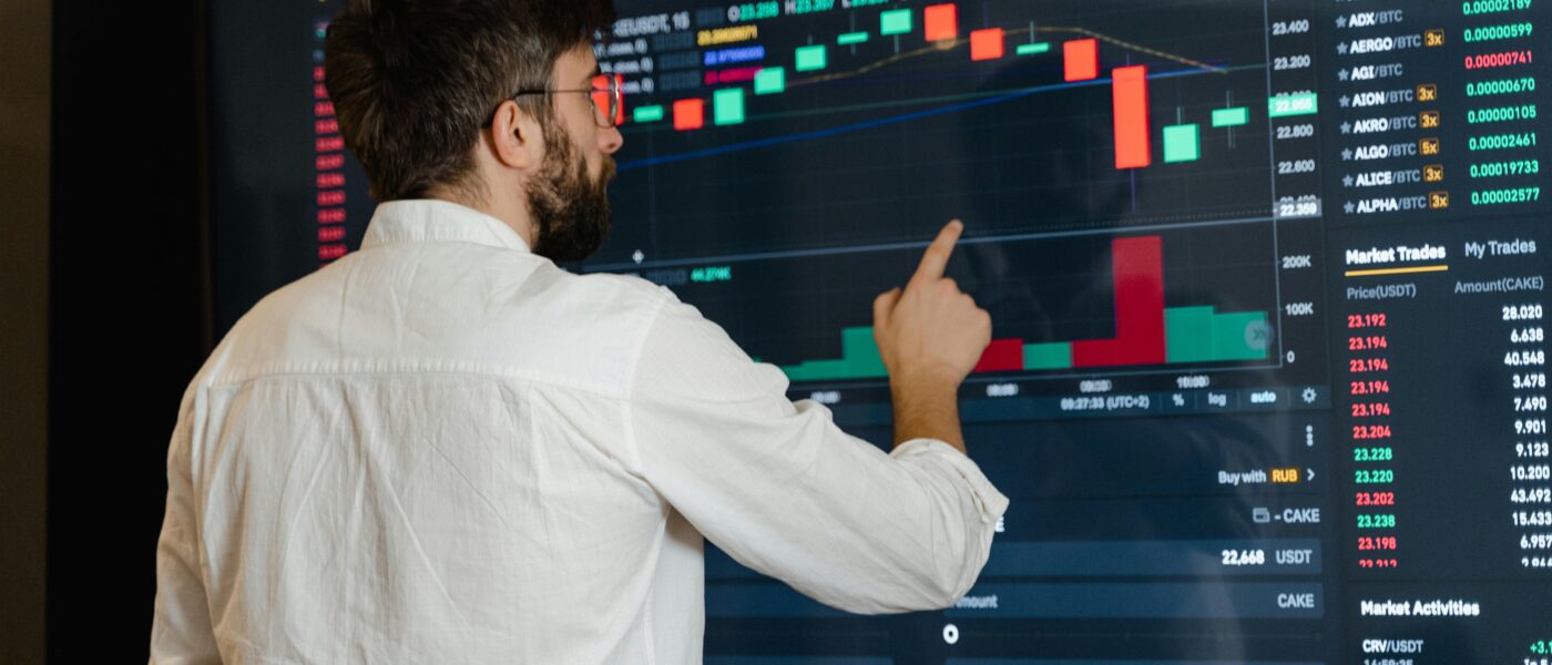 A man analyzes cryptocurrency graphs on a touchscreen monitor in a modern office setting.