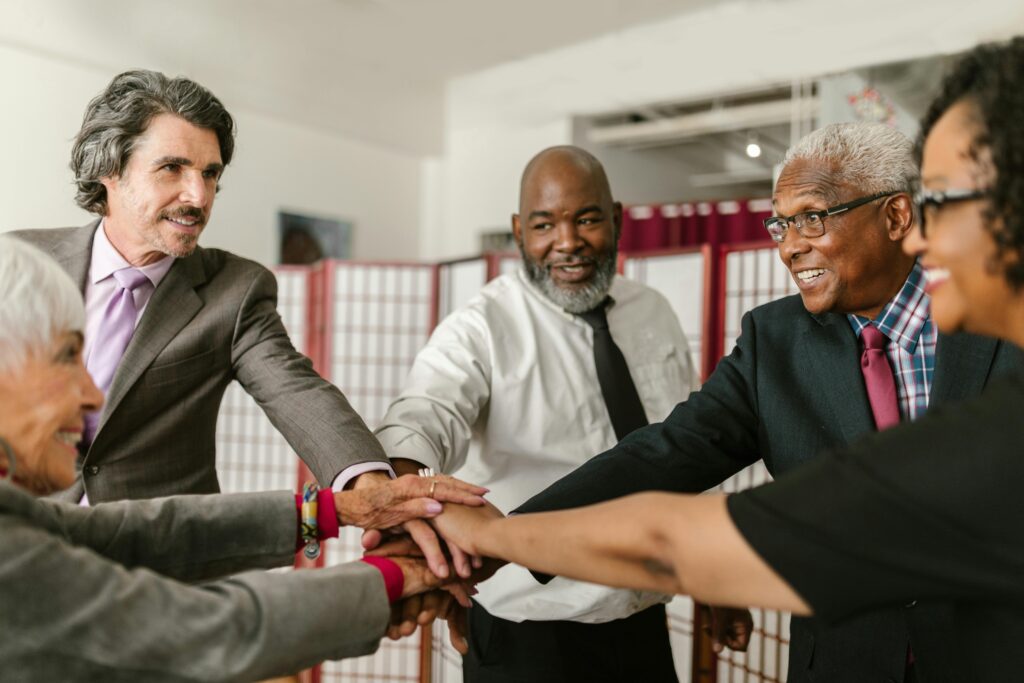 Senior business team showing unity with hands together, diverse colleagues smiling indoors.