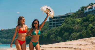 Two women in bikinis having fun at the beach on a sunny day, exuding joy and vacation vibes.