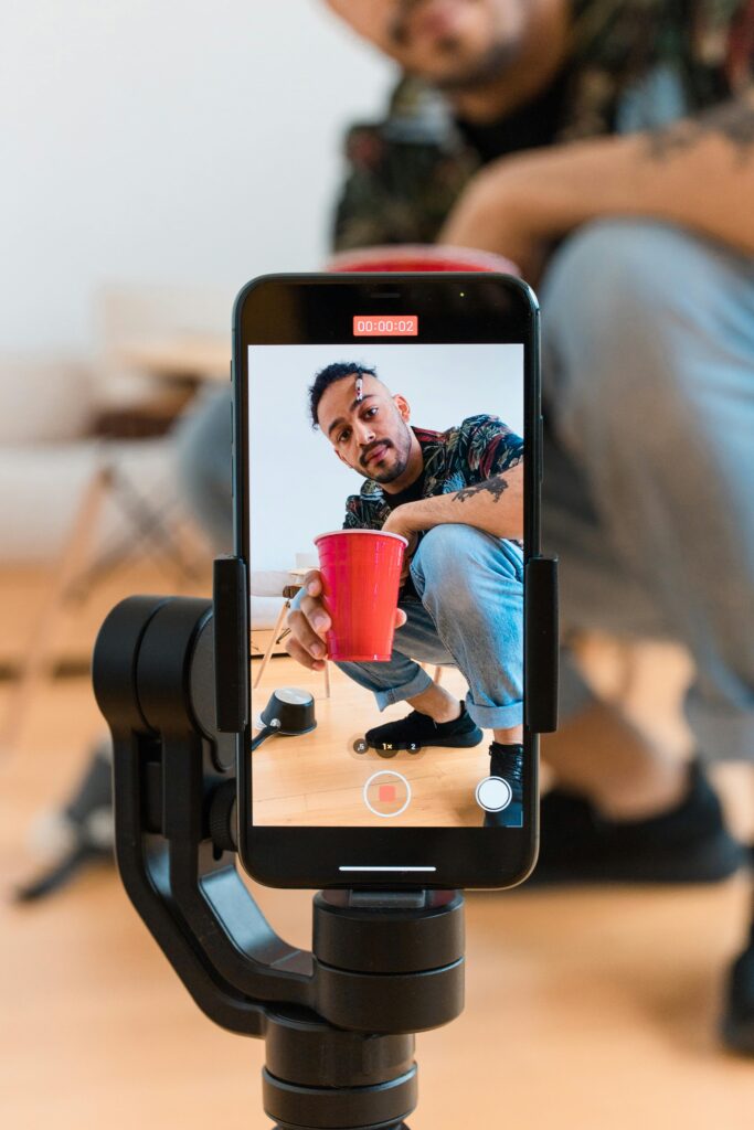 Man records a red cup trick using a smartphone mounted on a tripod.