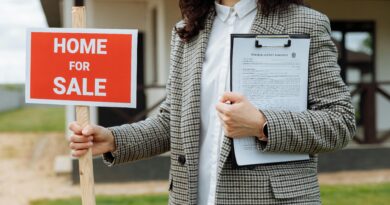 A real estate agent holding a home for sale sign and clipboard outside a property.