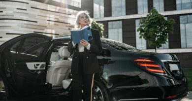 Senior businesswoman exits a black luxury car, holding documents near modern office building.