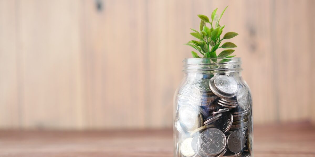 A jar of growing coins with a small plant, representing how to build wealth one asset at a time