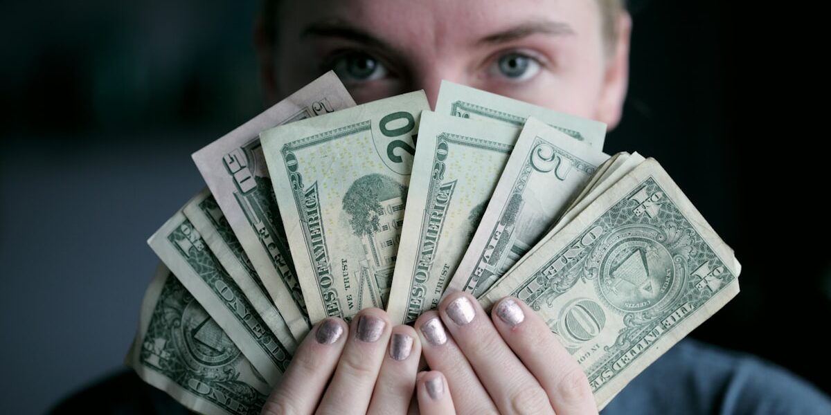 Person holding fanned-out dollar bills, representing how much to invest each month