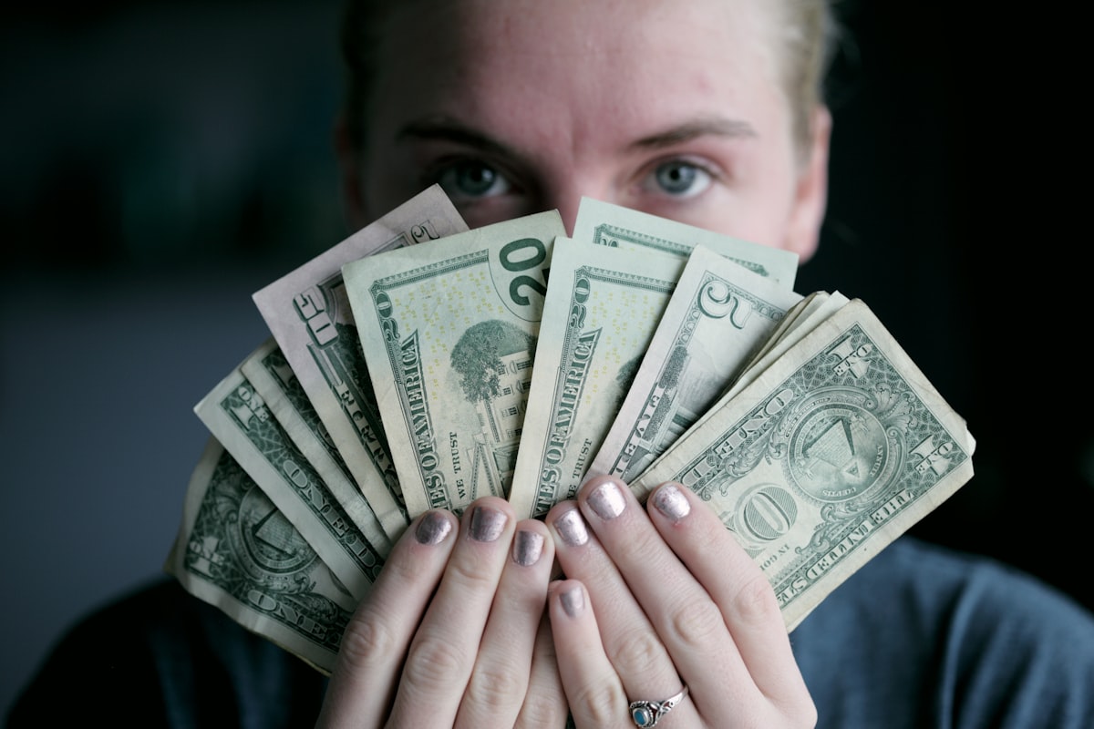 Person holding fanned-out dollar bills, representing how much to invest each month
