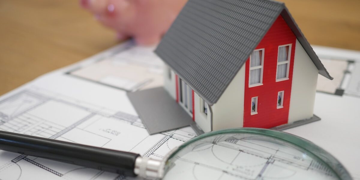 Miniature house model with a piggy bank and blueprint, representing how to start a rental property business with 10000 dollars