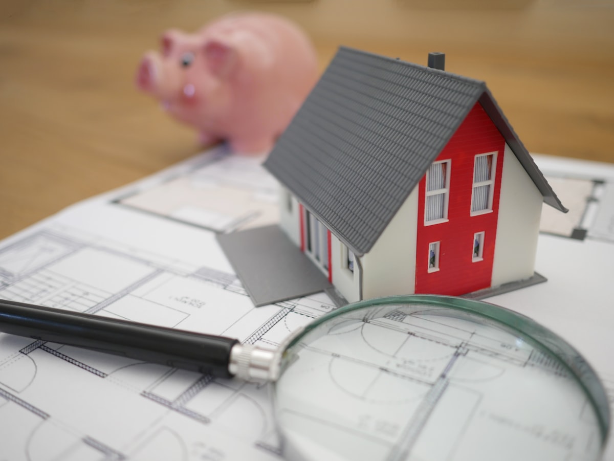Miniature house model with a piggy bank and blueprint, representing how to start a rental property business with 10000 dollars
